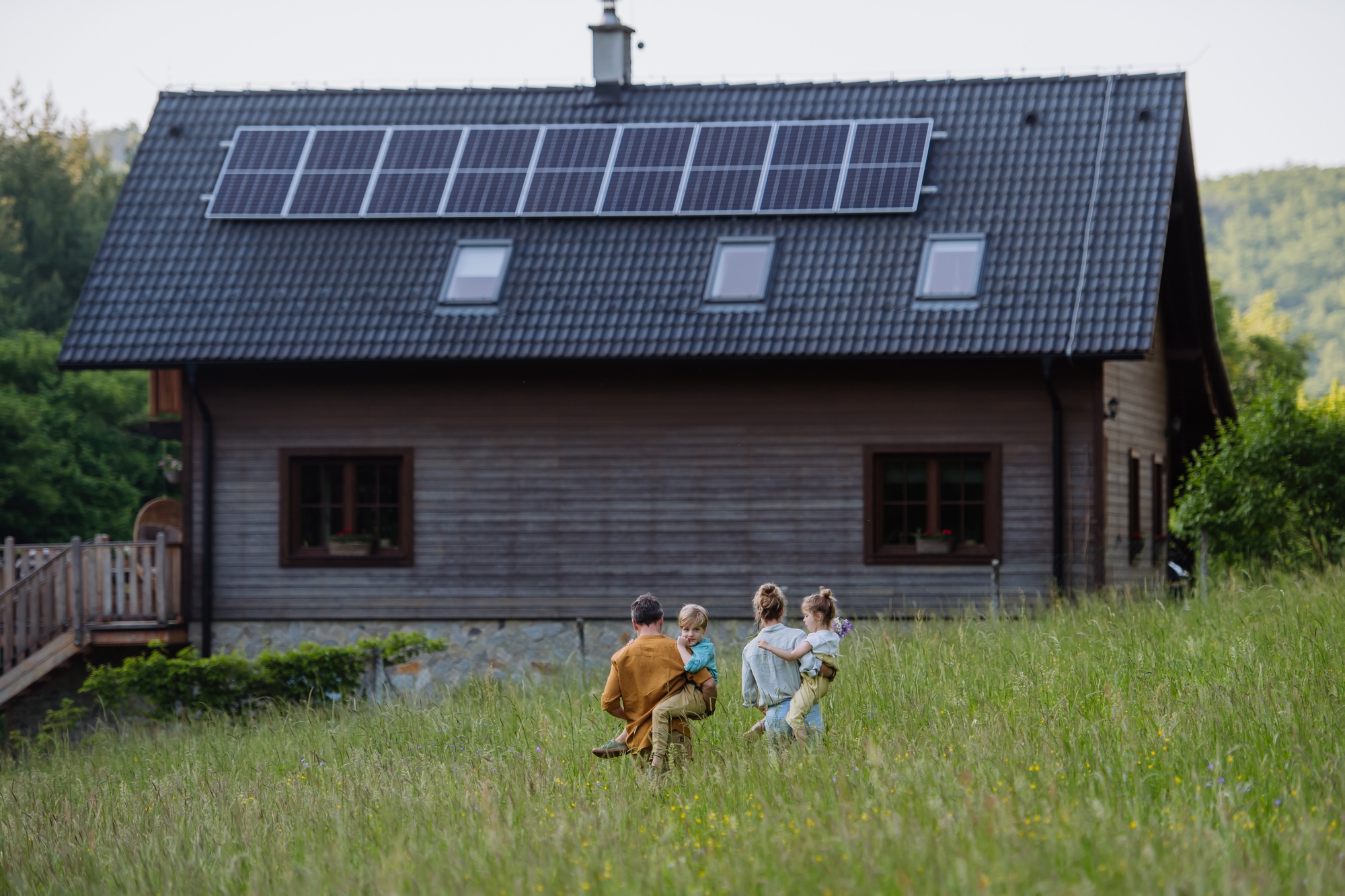 Happy family in front of their house with solar panels on the roof.